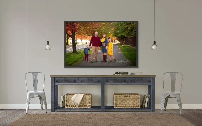Framed family portrait of four people walking a tree-lined autumn path, hung above a console table.